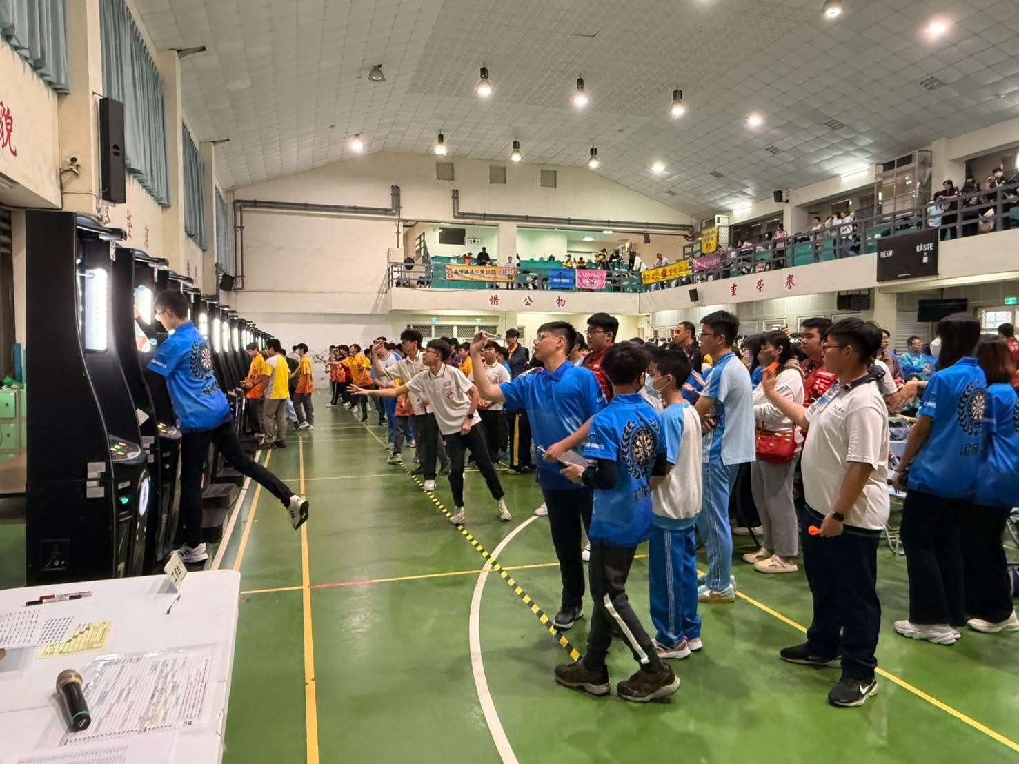 歷屆競技飛鏢賽事的現場實況回顧。照片中眾多參賽選手在整齊排列的電子飛鏢機台前專注投擲，展現飛鏢運動的高人氣與熱血氛圍。