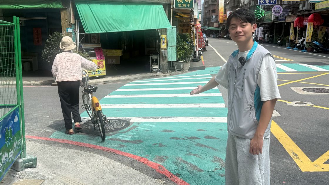 劉韋呈站在板橋海山里長安街138巷路口，伸手指向學生通行的斑馬線轉角